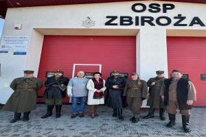 Zdjęcie: mężczyźni i kobiety stojący na tle bramy garażowej Ochotniczej Straży Pożarnej